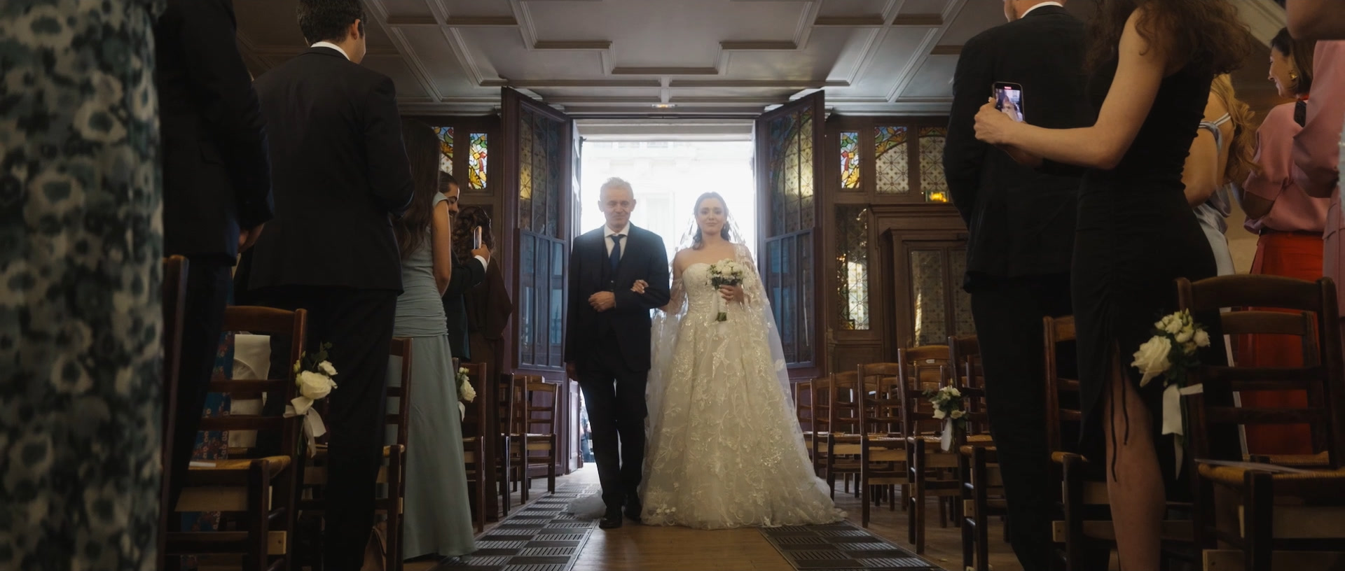 La mariée entre dans l'église au bras de son père, entre les invités debout